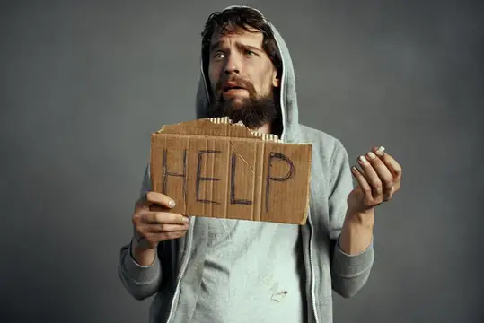 Бородатый мужчина в капюшоне держит картонный знак с надписью HELP