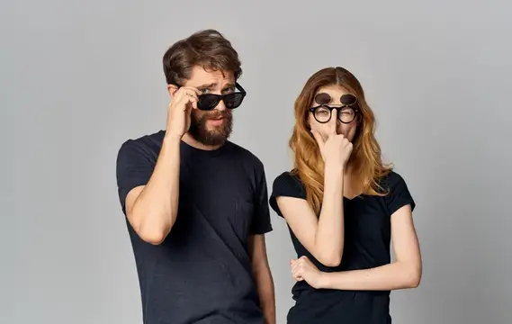 Мужчина и женщина в солнцезащитных очках дурачатся на сером фоне