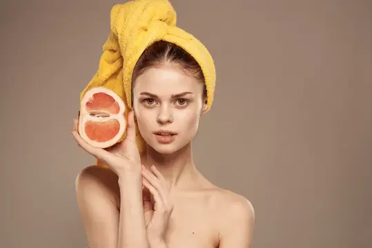 Симпатичная женщина с полотенцем на голове, чистая кожа, оголённые плечи, цитрусовый фрукт в руках