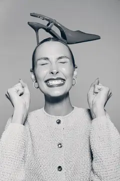 Улыбающаяся женщина с туфлей на голове держит кулаки у лица