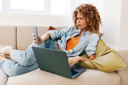 Улыбающаяся женщина работает за ноутбуком в уютной современной гостиной