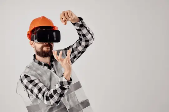Строитель в оранжевой каске и VR-очках жестикулирует на сером фоне