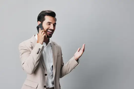 Молодой мужчина в деловом костюме, улыбаясь, держит в руке смартфон и разговаривает по нему