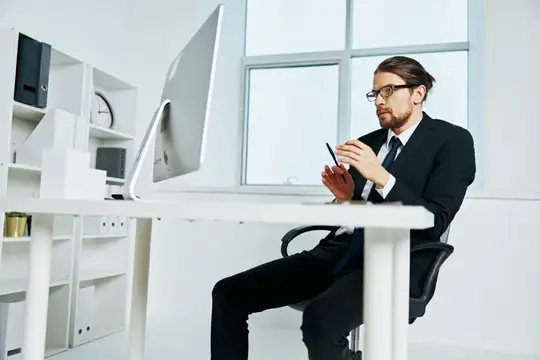 Мужчина в очках и костюме работает за компьютером в светлом офисе