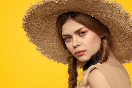 Молодая девушка в соломенной шляпе с косичками на жёлтом фоне