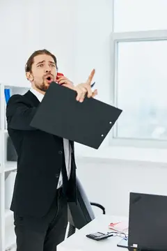 Мужчина в костюме с папкой эмоционально говорит по телефону в офисе