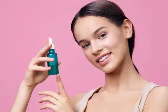 Улыбающаяся девушка держит флакон сыворотки на розовом фоне