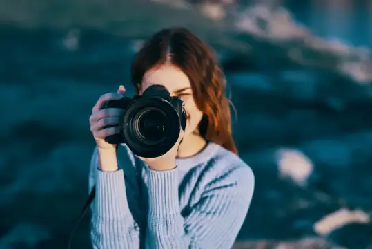 Молодая девушка фотографирует на камеру у синей воды