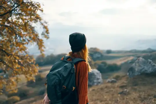 Девушка с рюкзаком смотрит на осенние холмы