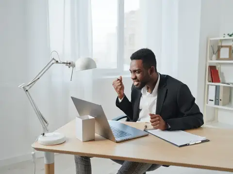 Улыбающийся темнокожий мужчина в костюме работает за ноутбуком в офисе