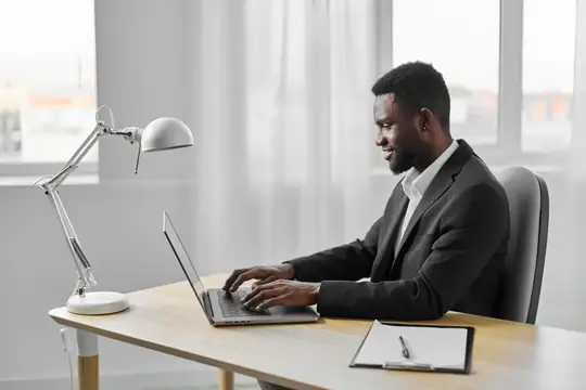 Темнокожий мужчина в костюме работает за ноутбуком в светлом офисе