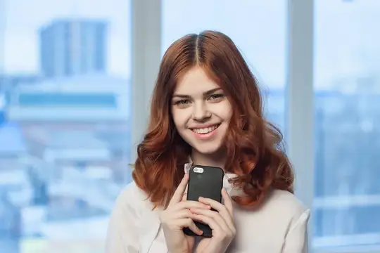 Веселая рыжеволосая женщина с телефоном в руках общается в официальном офисе