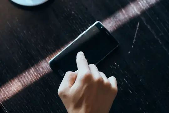 Рука с указательным пальцем на экране смартфона на тёмном столе