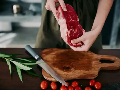 Повар держит кусок сырого мяса над деревянной доской