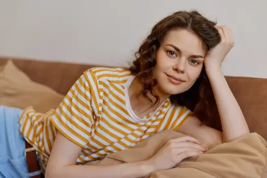 Кудрявая девушка в полосатой футболке лежит на диване и улыбается