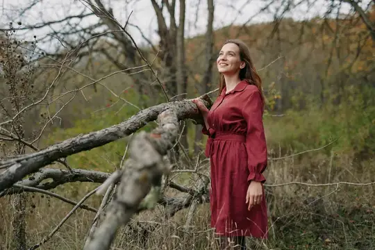 Улыбающаяся женщина в бордовом платье у поваленного дерева в осеннем лесу
