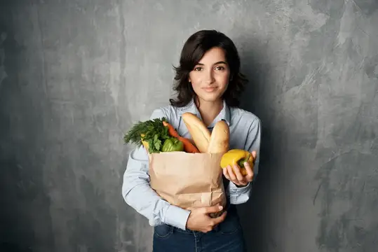 Женщина с пакетом продуктов, овощами, здоровой пищей, снятая в студии на фоне супермаркета