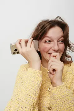 Молодая женщина в желтом свитере кокетливо говорит по телефону