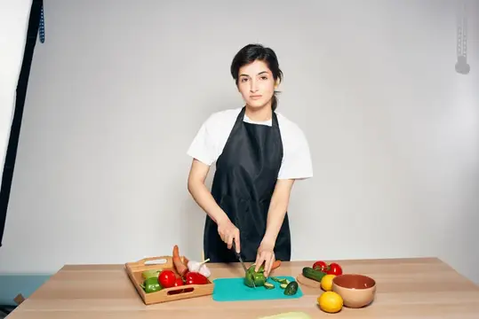 Молодая женщина в фартуке режет овощи на кухне