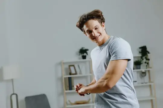 Улыбающийся парень в футболке танцует в светлой комнате