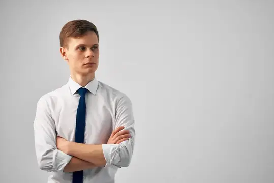 Молодой человек в белой рубашке и галстуке стоит со скрещёнными руками