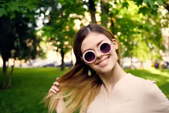Улыбающаяся девушка в круглых солнцезащитных очках в летнем парке