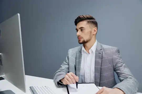 Красивый мужчина с документами на столе работает за компьютером, испытывая эмоции руководителя