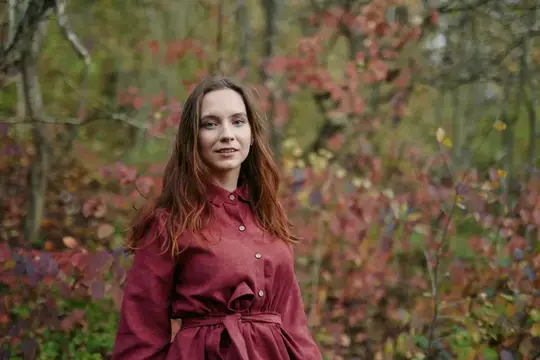 Молодая женщина в бордовом платье на фоне осеннего леса