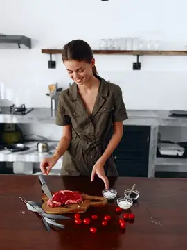 Улыбающаяся девушка готовит стейк с помидорами на кухне
