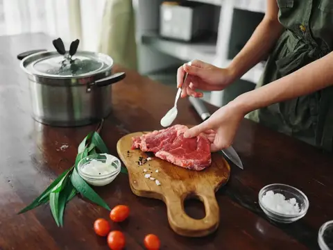 Женщина на кухне готовит ужин из мяса, овощей и специй на деревянном столе на фоне стильной кухни, крупным планом руки, свежие экопродукты, образ жизни
