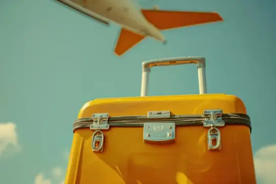 Желтый чемодан на фоне взлетающего самолета