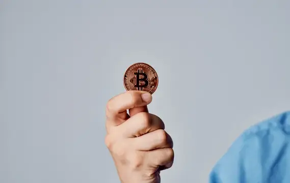 Рука держит золотую монету биткоин на сером фоне