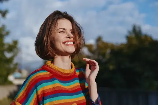 Улыбающаяся девушка с каре в разноцветном свитере на улице