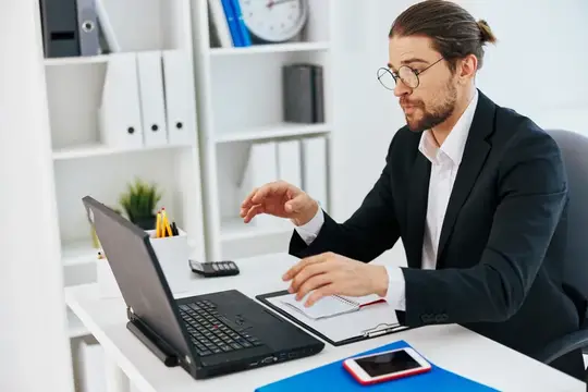 Мужчина с длинными волосами в очках работает за ноутбуком в офисе