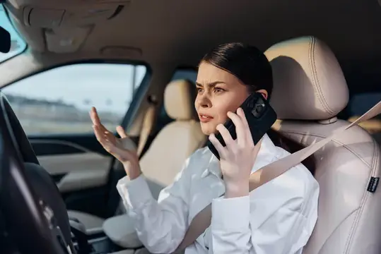 Женщина за рулём говорит по телефону и жестикулирует