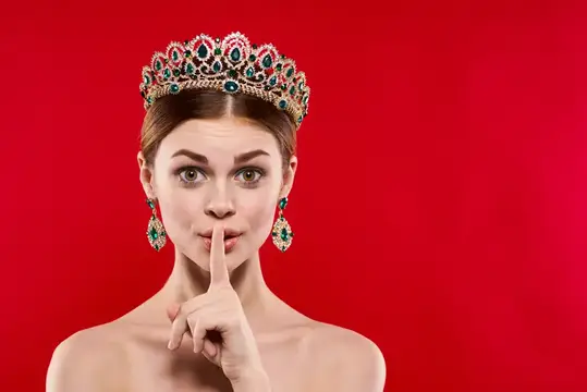 Молодая женщина в короне прикладывает палец к губам на красном фоне