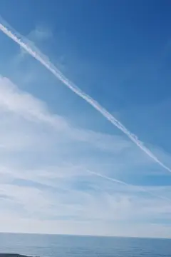 Белый след самолёта в ясном небе над морем
