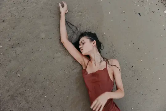 Молодая женщина лежит на песке с вытянутой рукой