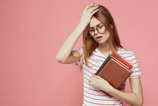 Молодая студентка с книгами на розовом фоне, в очках на лице, кадрированный вид, учебное заведение
