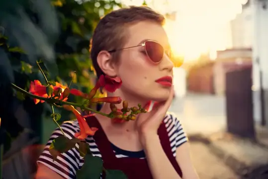 Стриженая девушка в солнцезащитных очках у цветущего куста