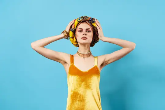 Рыжеволосая женщина в жёлтом платье поправляет яркий тюрбан на голове
