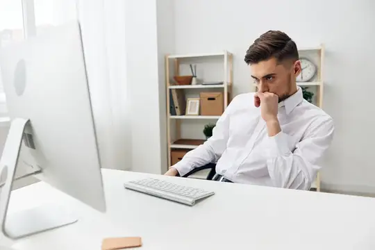 Задумчивый мужчина в белой рубашке работает за компьютером в офисе