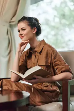 Задумчивая девушка с книгой у окна в коричневом платье