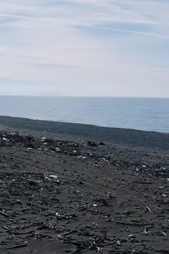 Берег из черного песка у океана, тихие волны и далекий горизонт, каменистая галька вдоль побережья, безмятежный морской пейзаж для любителей природы, тем окружающей среды или отдыха