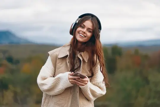 Улыбающаяся девушка в наушниках слушает музыку на природе