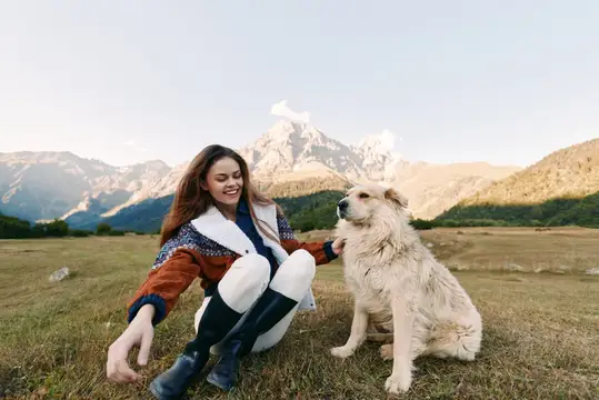 Женщина и собака на лугу в горах, гладит пушистого компаньона, улыбаясь на открытом воздухе