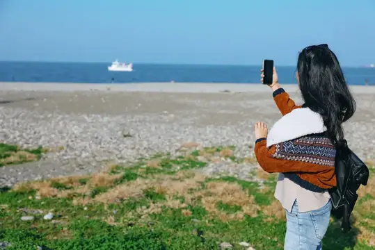 Девушка фотографирует море и корабль со скалистого берега