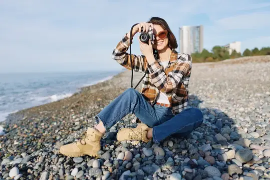 Девушка в клетчатой рубашке фотографирует на камеру у моря