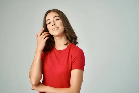 Молодая темноволосая женщина в красной футболке поправляет волосы