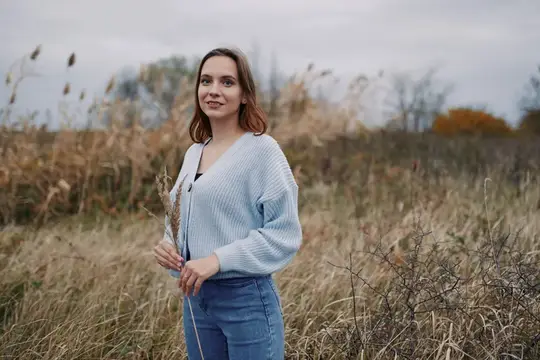Молодая женщина в голубом свитере стоит в осеннем поле